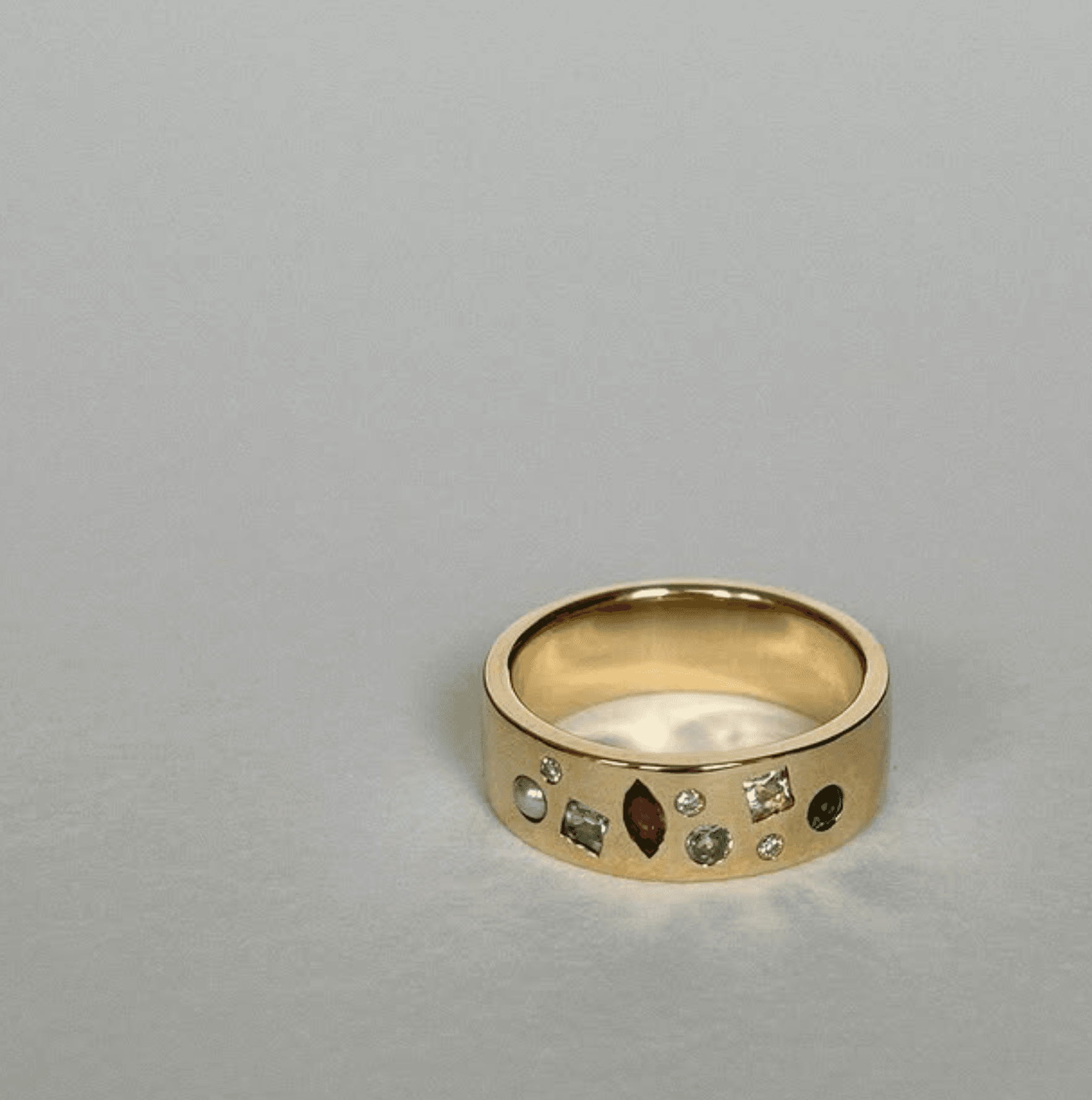 Wide 18ct yellow gold band flush-set with mixed heirloom stones - marquise ruby, round emerald, aquamarine, and old-cut diamonds - on a soft grey surface